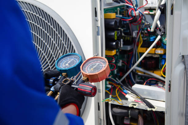 A technician in blue uniform uses pressure gauges to inspect an open HVAC unit filled with colorful wires, conveying a sense of focus and technical expertise.